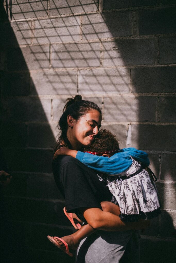 A touching scene of a mother holding her sleeping child in a sunlit urban setting.