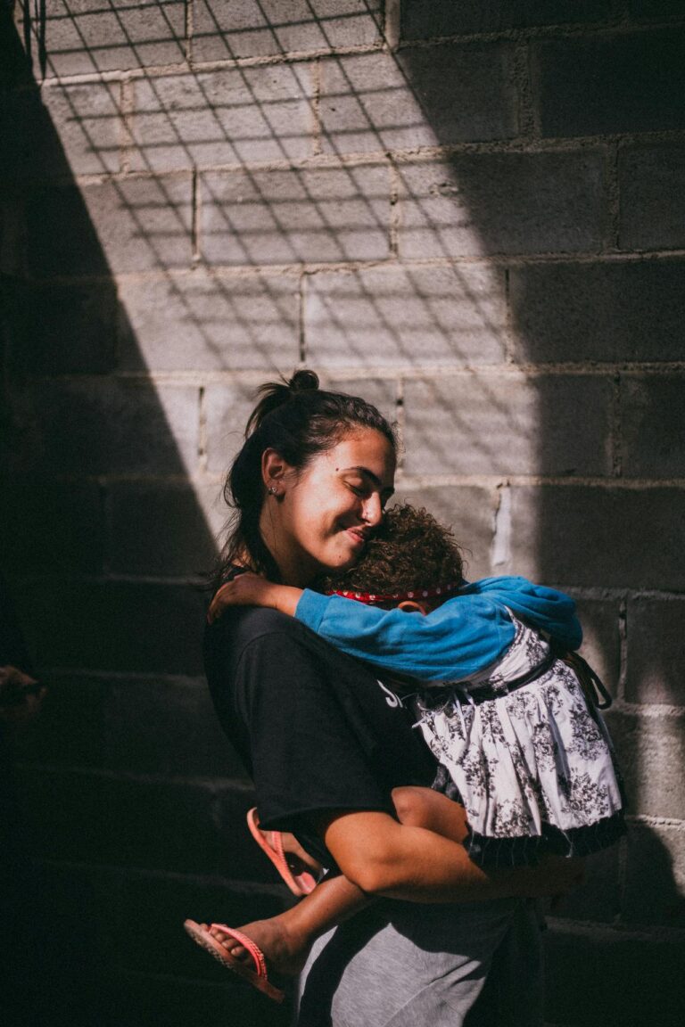 A touching scene of a mother holding her sleeping child in a sunlit urban setting.